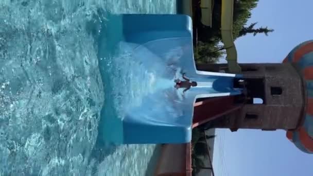 Happy kids riding down a water slide Dzieci bawią się w aquaparku podczas wakacji na świeżym powietrzu pionowo - Materiał filmowy, wideo