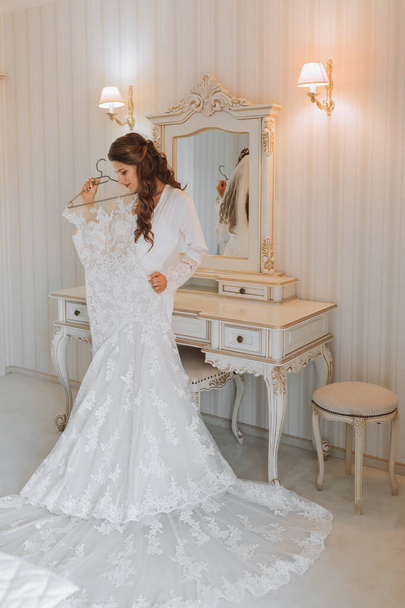 白いペチコートの美しい若い花嫁が立って,彼女の手にウェディングドレスを保持しています. 結婚式のための最終準備. 花嫁は花嫁を待っている. 朝から花嫁. - 写真・画像