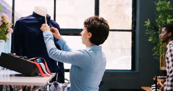 Zaměstnanec uzavírá knoflíky košile, zařizuje stylové zboží v moderním butiku. Bělošský manažer pracující v obchodě vizuální, kontrola ramínka plná nové módní kolekce v nákupním centru - Fotografie, Obrázek