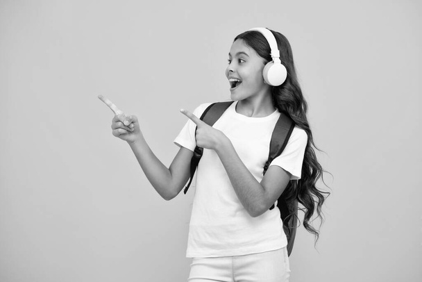 Chica adolescente asombrada. Chica de la escuela en auriculares sobre fondo de estudio aislado. Concepto de escuela y música. Excitada expresión, alegre y alegre - Foto, imagen