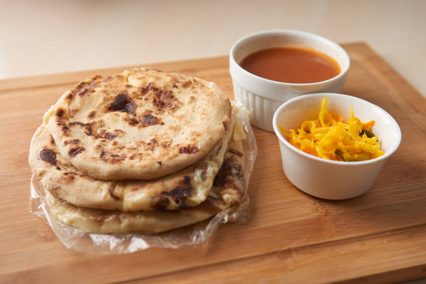 Central America traditional pupusas, a flavorful delight from El Salvador, Honduras, and Nicaragua, served with curtido and sauce on a rustic wooden tray - Photo, Image
