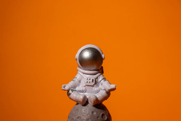 Plastic toy astronaut on colorful orange background Copy space. Concept of out of earth travel, private spaceman commercial flights. Space missions and Sustainability - 写真・画像