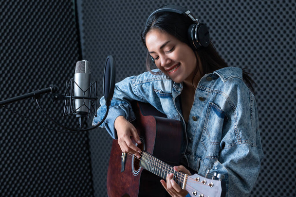 Happy cheerful pretty smiling of portrait a young Asian woman vocalist Wearing Headphones with a Guitar recording a song front of microphone in a professional studio - Valokuva, kuva