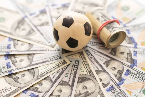Leder-Fußballball auf dem Feld der Hintergrund-Papier-Dollarscheine. Hochwertiges Foto - Foto, Bild