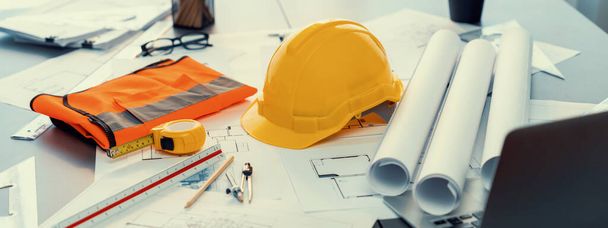 Architectural designed building blueprint layout and engineer tool for designing blueprint with contractor project document on engineer workspace table in office with safety helmet or hardhat. Insight - Photo, Image