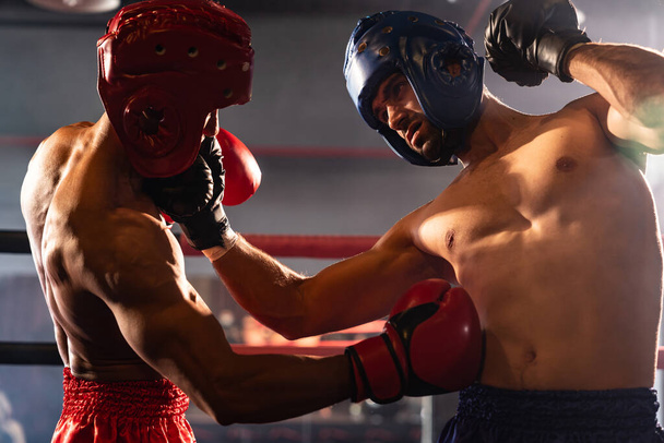 Two athletic and muscular body boxers with safety helmet or boxing head guard face off in fierce boxing match. Boxing fighter competitor fighting in the boxing ring. Impetus - Photo, Image