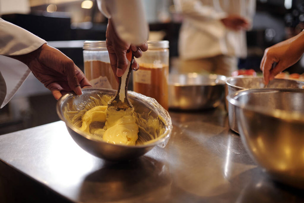 Close-up beeld van kok slaan zuivel boter en zout in metalen kom - Foto, afbeelding