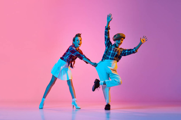 Beautiful, artistic, emotive children in retro stylish clothes dancing against pink studio background in neon light. Concept of childhood, hobby, active lifestyle, performance, art, fashion - Photo, Image
