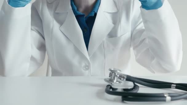 Gezondheidszorg in actie: een medisch specialist in een witte jas, doet een stethoscoop aan en bereidt zich voor op een medisch onderzoek. De arts zet een beschermend masker voor een ontmoeting met de patiënt in de - Video