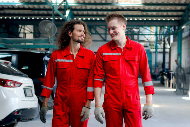 Two handsome mechanic men in red uniform walking through row of vehicle at garage, auto mechanic technician friend work together to repair and maintenance customer car automobile at car service shop. - Valokuva, kuva