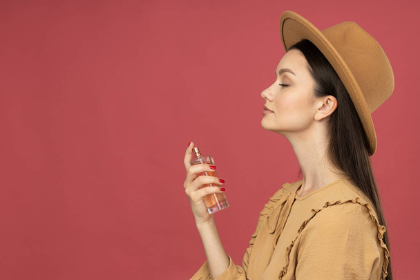 Mujer joven en sombrero aplicando perfume sobre fondo rosa, espacio para texto - Foto, imagen