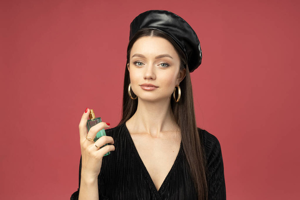 Young woman in beret with perfume bottle on pink background - Photo, Image