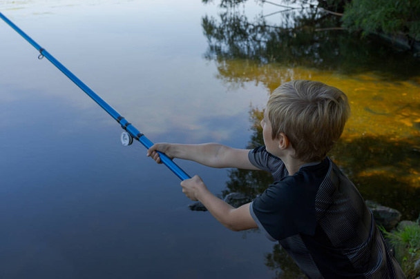 Un adolescent sur une rivière jette une canne à pêche pour attraper le poisson. Pêche sportive sur la rivière en été. - Photo, image