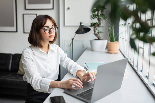 Zamyślony bizneswoman patrząc na laptopa koncentruje się na pracy online, siedzi przy stole w przestrzeni współpracowników, przestrzeń kopiowania. Zajęta kobieta surfing web myślenie o problemach w miejscu pracy z komputerem - Zdjęcie, obraz