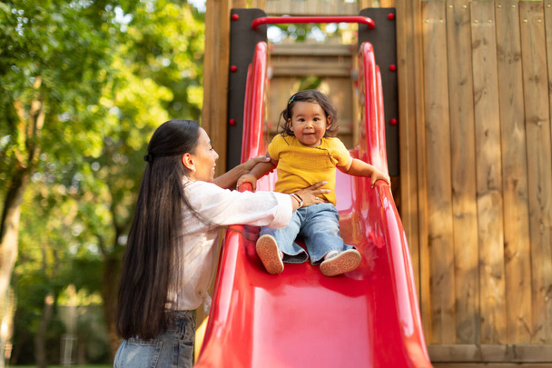Kisgyerek Kaland Kint. Boldog japán kisbaba lánya Élvezi Játszótér Szórakozás Anyával, Anya Catching csecsemő, ahogy lovagol le a csúszdák a parkban szabadban - Fotó, kép