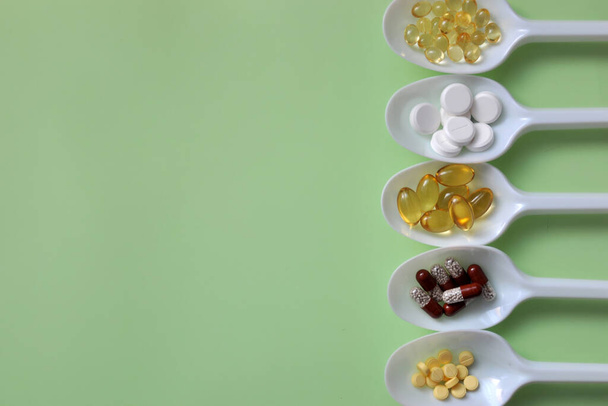 Tabletit, kapselit, ravintolisät, vitamiinit valkoisissa lusikoissa. Lääketieteellinen tausta pillereitä - Valokuva, kuva