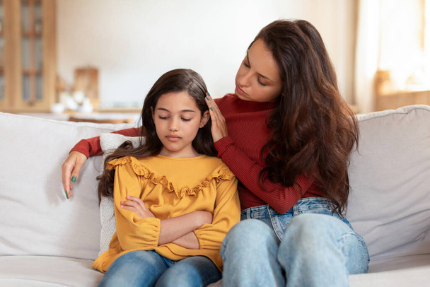 Kwestia depresji dzieci. Wspierająca arabska mama rozmawiająca z nieszczęśliwą córką, wspierająca ją w dziecięcych zmaganiach, siedząca na kanapie i przytulająca w domu. Kid koncepcja problemu psychicznego - Zdjęcie, obraz