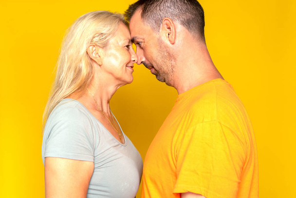 Romantyczna kaukaska para po czterdziestce szczęśliwa dotykając czoła i patrząc sobie w oczy, odizolowana na żółtym tle studia - Zdjęcie, obraz