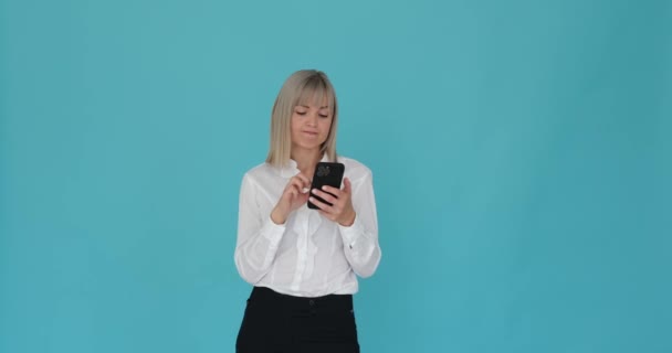 Mujer de negocios aburrida se muestra bostezando mientras sostiene su teléfono contra un fondo azul calmante. Su cansada expresión y gesto bostezante indican su falta de interés o compromiso con el dispositivo. - Imágenes, Vídeo