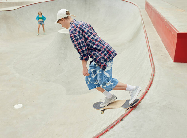 Teen boy in checkered shirt skateboarding on skate park, having fun and active leisure time with friends. Concept of youth culture, sport, dynamic, extreme, hobby, action and motions, friendship - Fotó, kép
