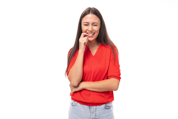 giovane gentile affascinante signora bruna vestita con una t-shirt rossa sorride dolcemente su uno sfondo bianco. - Foto, immagini
