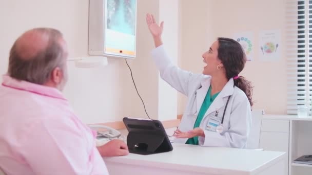 Üniformalı kadın doktorlar, klinikteki sağlık kontrollerinden ve sağlık randevularından sonra beyaz erkek hastalara X-ray film fiziksel muayenesi hakkında bilgi verir ve tavsiyelerde bulunurlar.. - Video, Çekim