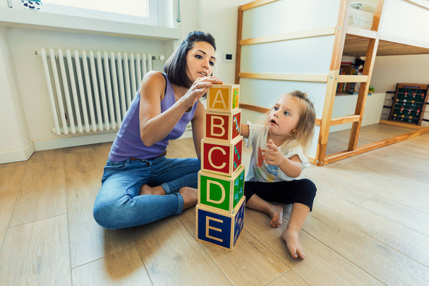 Dans une pièce remplie de jouets en bois, une jeune femme et sa fille blonde se lient, explorent et apprennent tout en s'amusant - Photo, image
