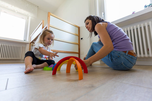 Coller sur des jouets en bois, une mère et sa fille blonde chérissent des moments d'apprentissage ludiques dans la chambre de l'enfant - Photo, image