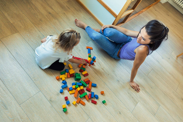Máma a dcera si hrají v místnosti plné dřevěných barevných hraček, stolů, bloků, zvýšení kreativity, baví, učení se spolu - Fotografie, Obrázek
