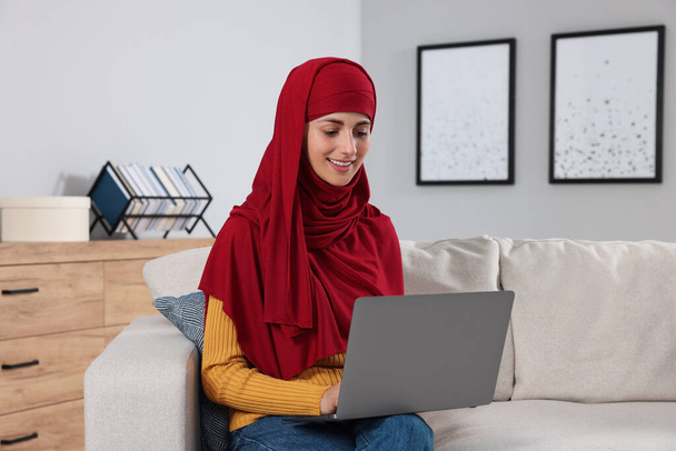 Muslim woman using laptop at couch in room - Photo, image
