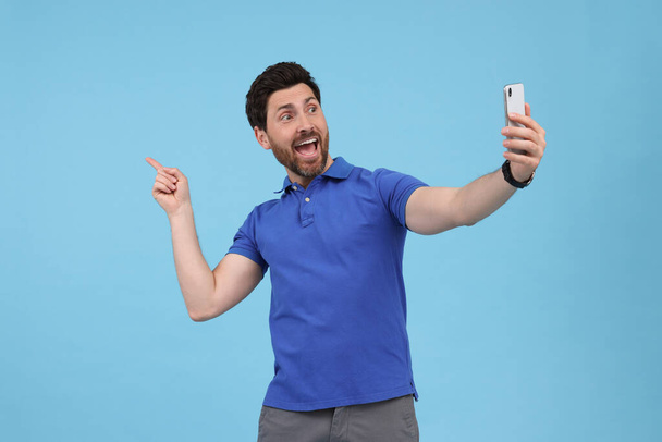 Happy man taking selfie with smartphone on light blue background - Foto, afbeelding