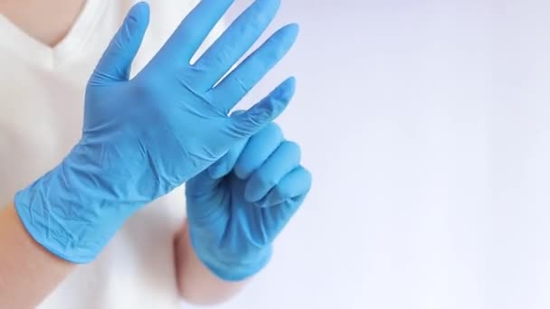 Handen in latex medische handschoenen. De dokter doet rubber blauwe handschoenen op de handen op een lichte achtergrond, close-up. Het concept van geneeskunde en gezondheidszorg. Arts of verpleegkundige draagt nitrilbeschermende handschoen - Video