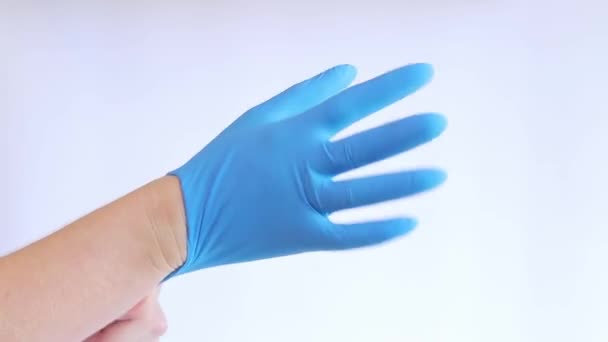 Kädet lateksikäsineissä. Lääkäri laittaa kuminsiniset käsineet käsiin kevyellä taustalla, lähikuva. Lääketieteen ja terveydenhuollon käsite. Lääkäri tai sairaanhoitaja, jolla on nitriilinen suojakäsine - Materiaali, video