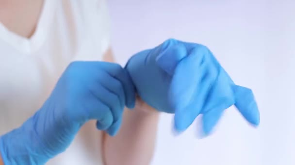 Handen in latex medische handschoenen. De dokter doet rubber blauwe handschoenen op de handen op een lichte achtergrond, close-up. Het concept van geneeskunde en gezondheidszorg. Arts of verpleegkundige draagt nitrilbeschermende handschoen - Video