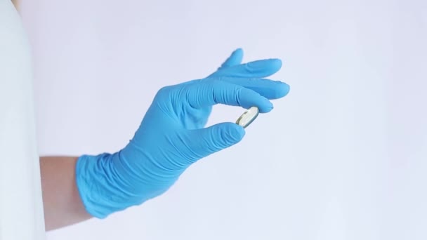 Egy kéz egy kék latex orvosi kesztyűben egy halolaj kapszulát tart. Az orvostudomány és az egészségügy fogalma, farmakológia. Az orvos vitaminokat mutat. Vitaminok és étrend-kiegészítők. Omega-3 halolaj kapszula - Felvétel, videó