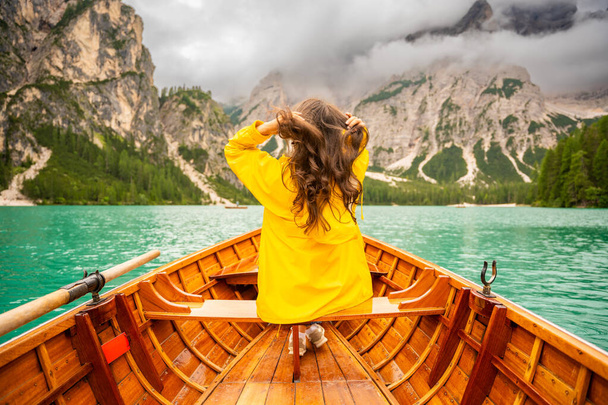 Женщина, сидящая в большой коричневой лодке на озере Лаго-ди-Брэйс в облачный день, Италия. Летние каникулы в Европе. Высокое качество фото - Фото, изображение