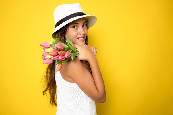 黄色の背景に隔離されたチューリップの大きな花束を保持するドレスで美しい若い女の子の肖像画 - 写真・画像