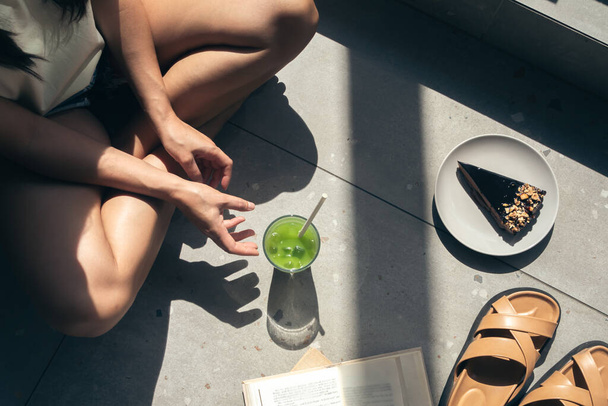 Composition estivale avec pantoufles, livres, gâteau et limonade dans les mains des femmes, ombres dures par une journée ensoleillée, vue sur le dessus. - Photo, image