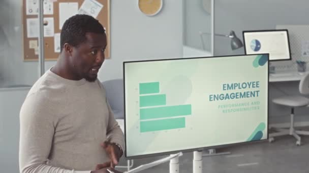 Zelfverzekerde jonge zwarte man maakt presentatie over de betrokkenheid van werknemers bij collega 's in modern kantoor - Video