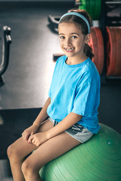Küçük kız spor salonunda fitness topuyla egzersiz yapıyor, çocuklar spor yapıyor ve spor yapıyor.. - Fotoğraf, Görsel