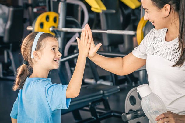 Mooie sterke vrouw en charmante kleine dochter geven high five in de sportschool. - Foto, afbeelding