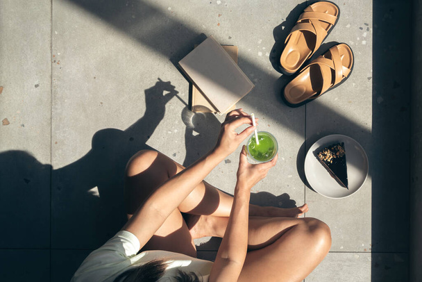 Composición de verano con zapatillas, libros, tarta y limonada en manos femeninas, sombras duras en un día soleado, vista superior. - Foto, Imagen