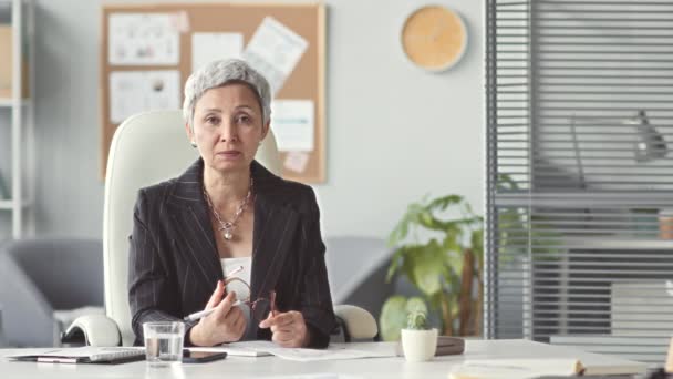 Steek taille omhoog shot van succesvolle volwassen Aziatische zakenvrouw spreken op camera terwijl zitten op het werk bureau in haar moderne kantoor - Video