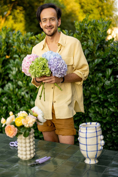 Portrait d'un homme joyeux arrange un bouquet avec des fleurs coupées dans le jardin. Homme fleuriste travaille dans son jardin à l'extérieur - Photo, image