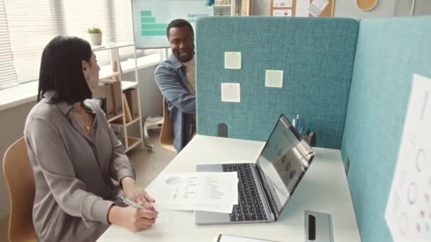 Twee diverse collega 's die door scheidingswand kletsen op hun werkplek - Video