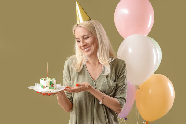 Зріла жінка з тортами на день народження та повітряними кулями на зеленому фоні - Фото, зображення