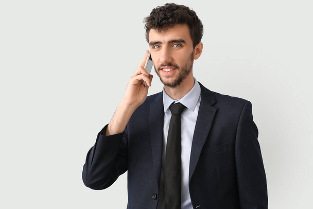 Young businessman in suit talking by mobile phone on light background - Photo, Image