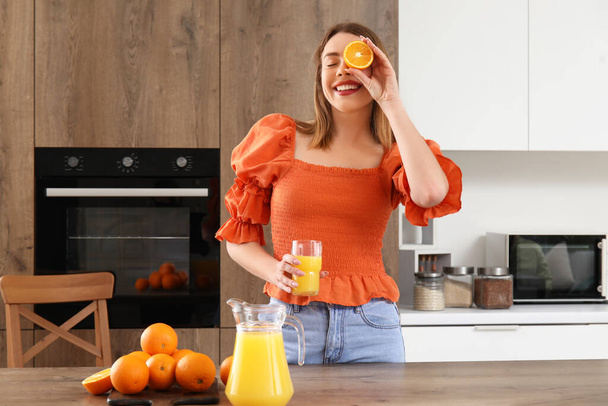 Jonge vrouw met glas sinaasappelsap in keuken - Foto, afbeelding