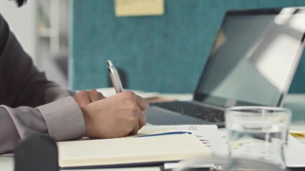 Sluiten van onherkenbare vrouwelijke kantoormedewerker schrijven notitie op sticker tijdens het zitten aan het bureau voor laptop computer - Video
