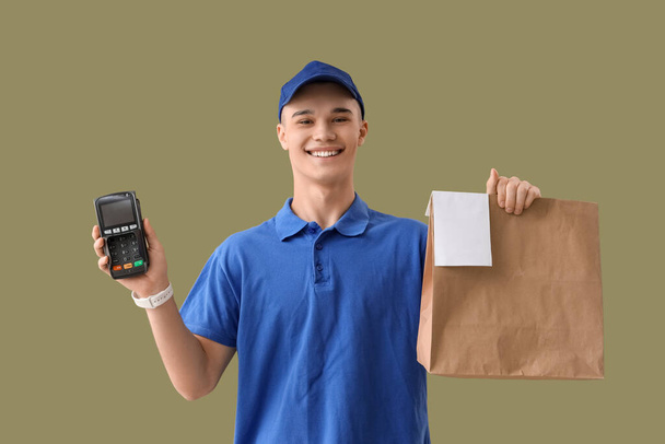 Young courier with paper bag and payment terminal on green background - Photo, Image